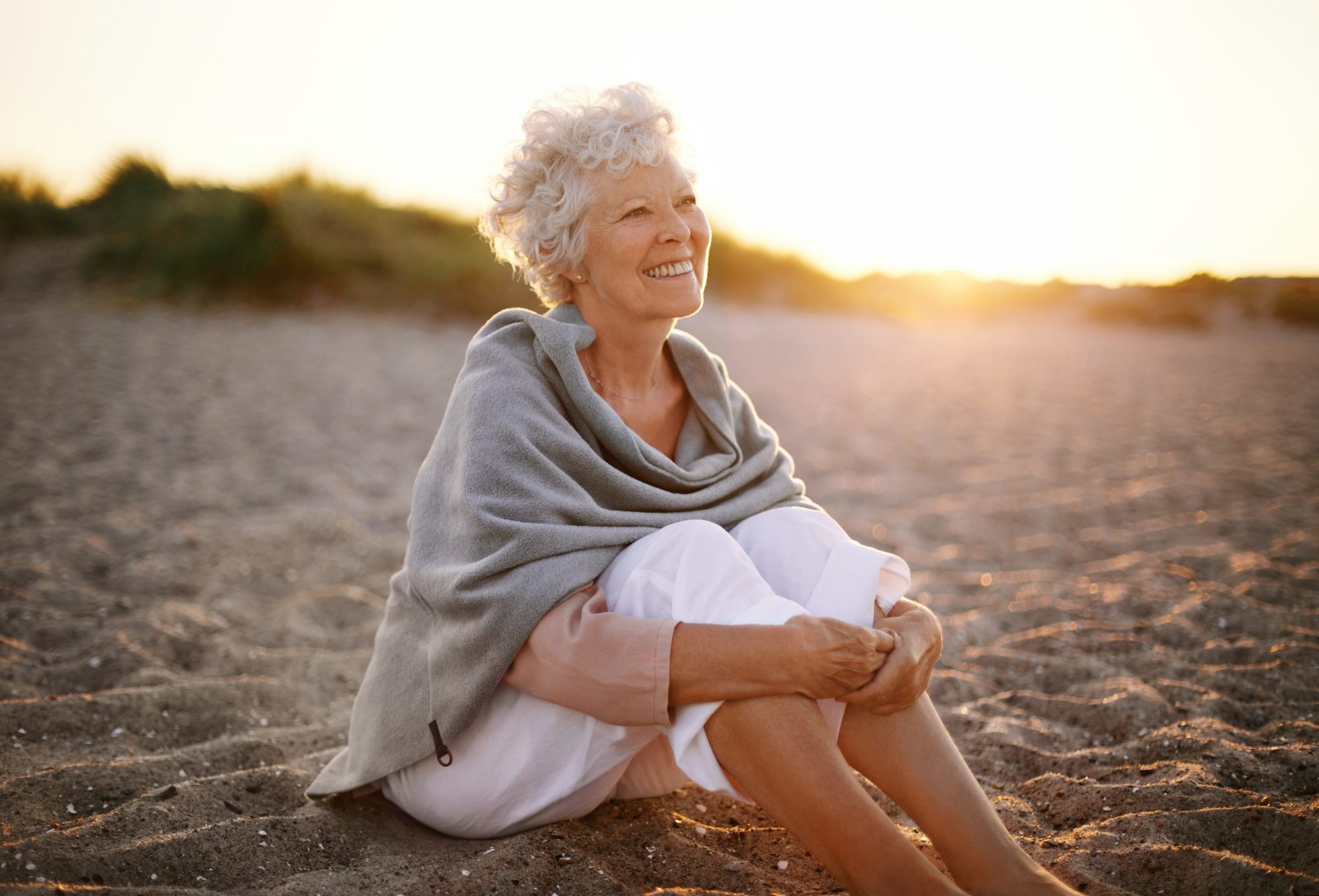 Happy retired woman wearing shawl sitting relaxed on the sand